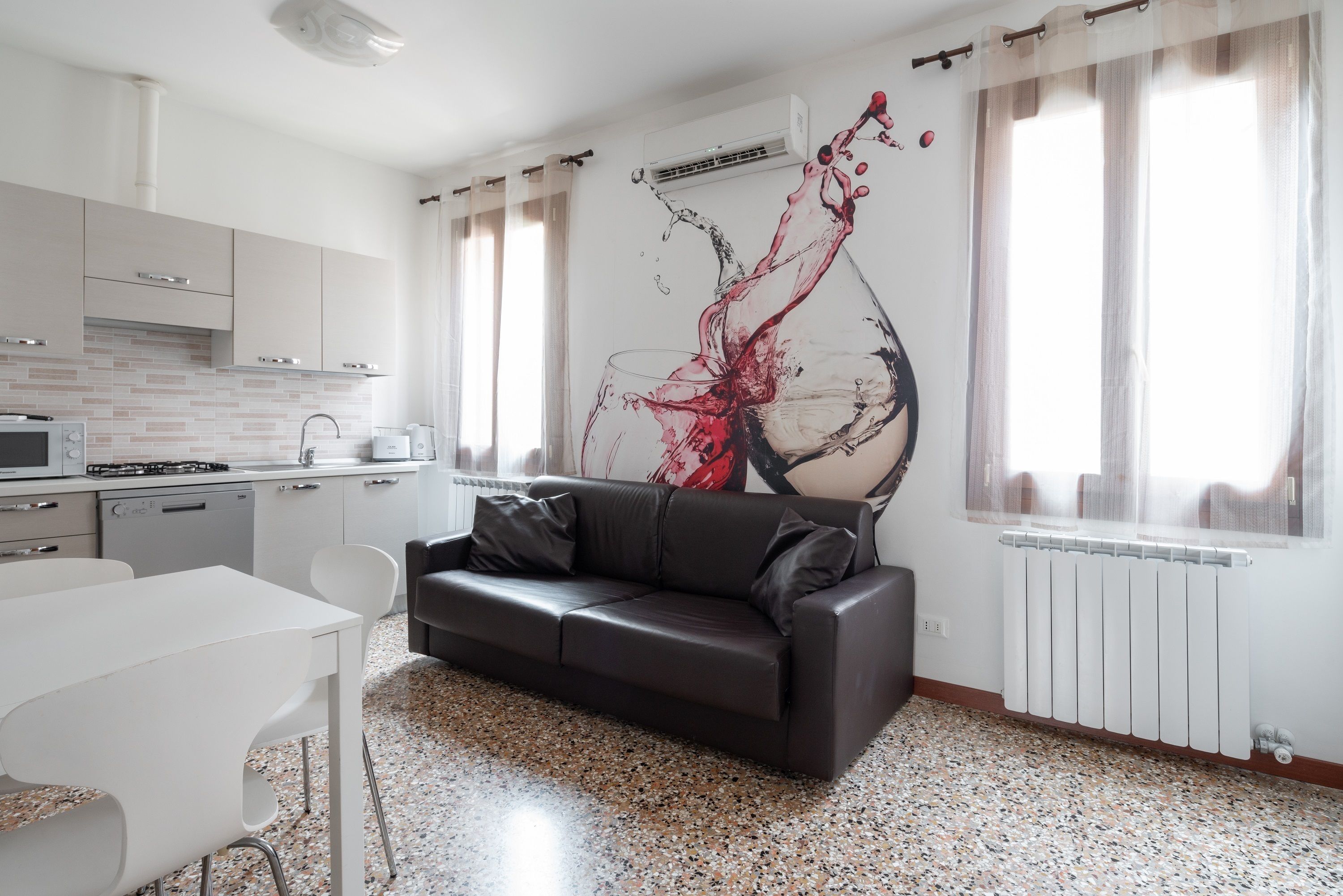 Une cuisine moderne avec des meubles blancs, un coin repas avec une table et des chaises blanches, et un canapé en cuir noir.