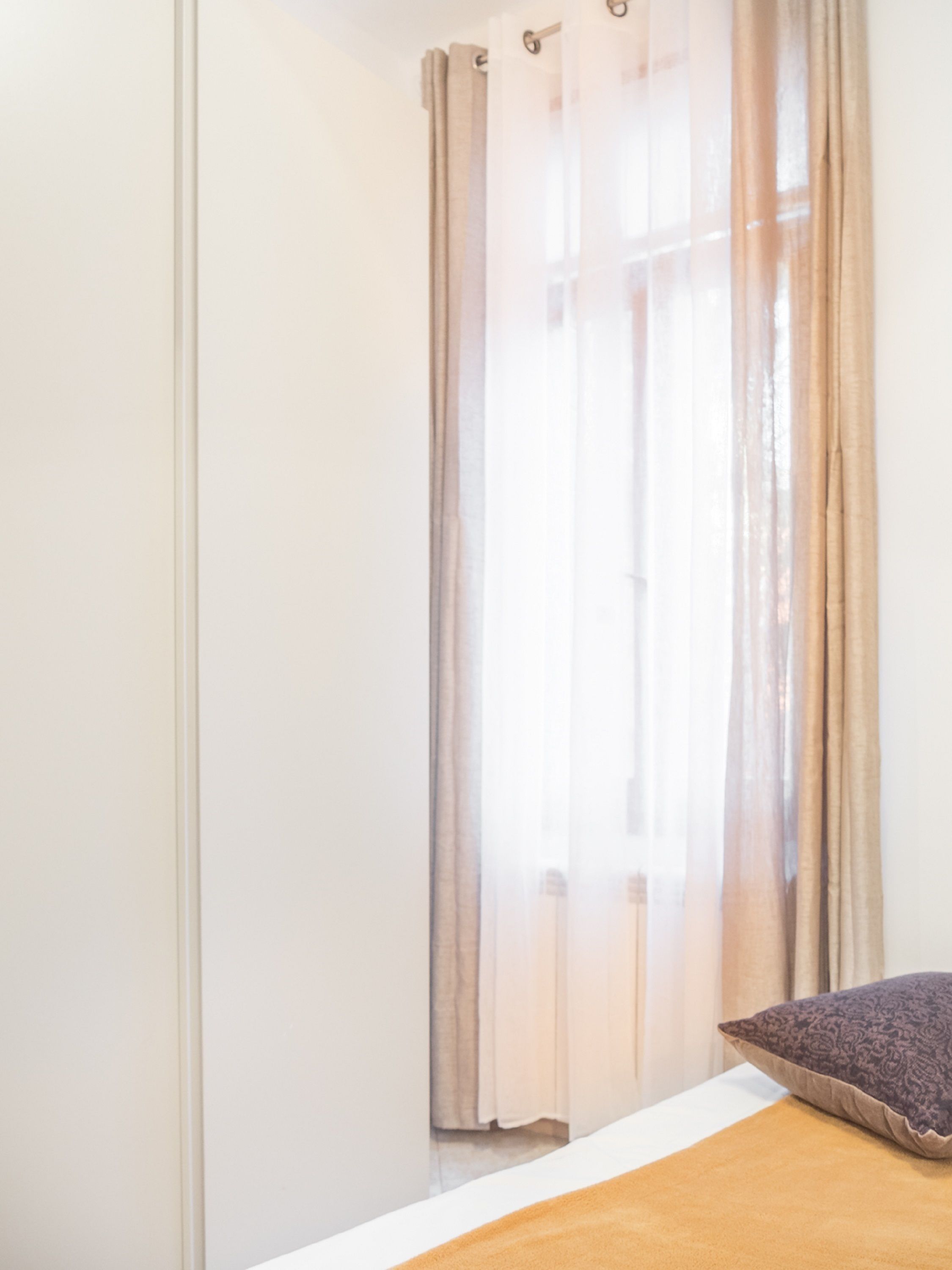 A room with a bed, a window with sheer curtains, and a pillow on the bed.
