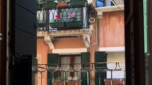 An open door with a view of a building's exterior, featuring a balcony with potted plants and a metal gate. - San Polo Canal View Apartments by Wonderful Italy (Venice)