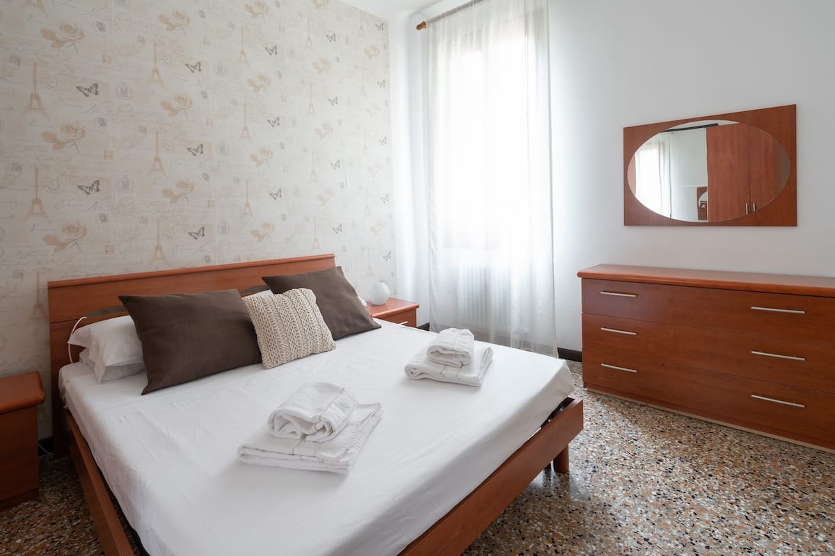 A neatly made bed with pillows, a wooden nightstand, a mirror, and a wooden dresser.