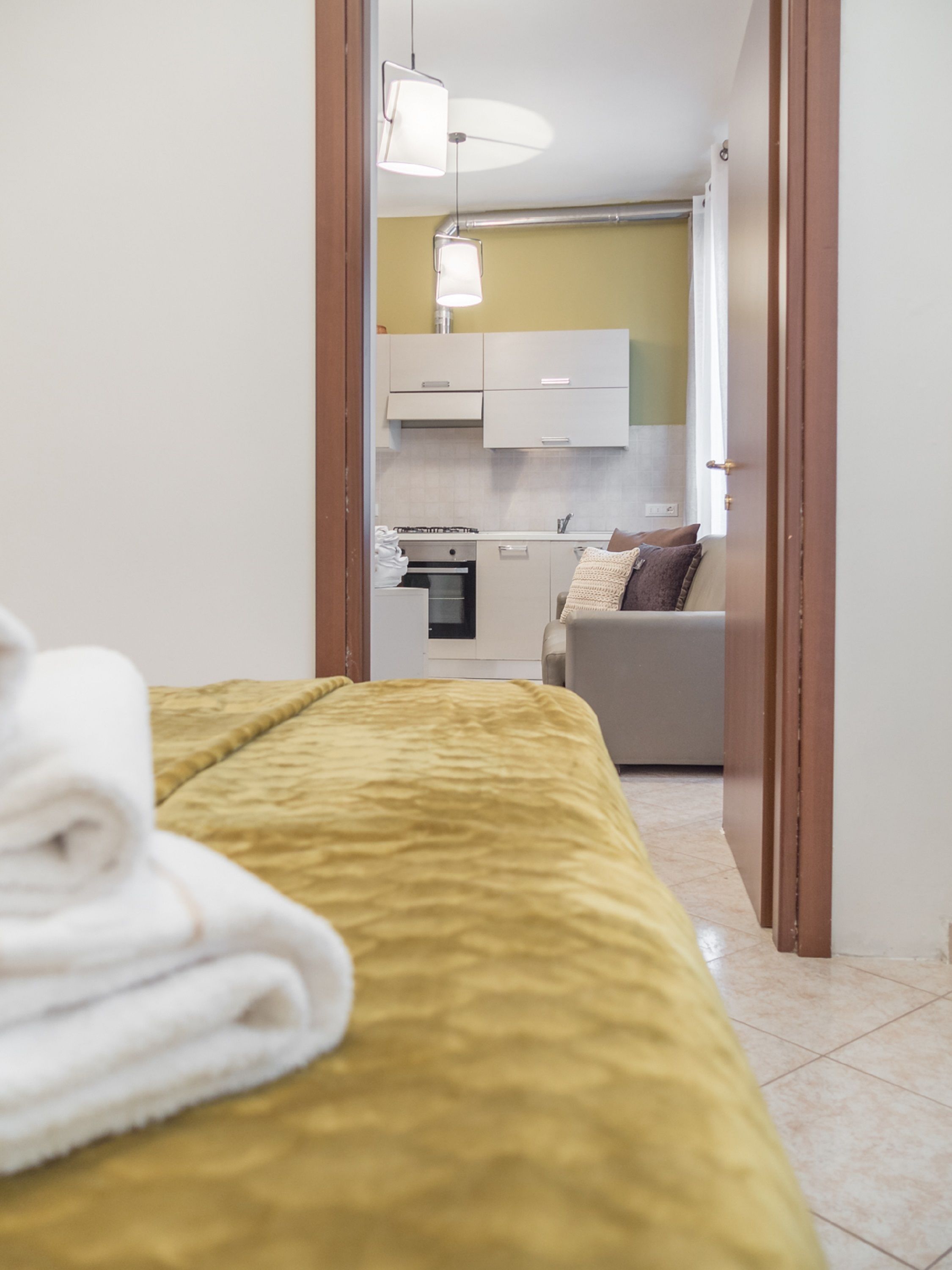A hotel room with a bed, a neatly folded towel, a kitchenette, and a sofa with cushions.
