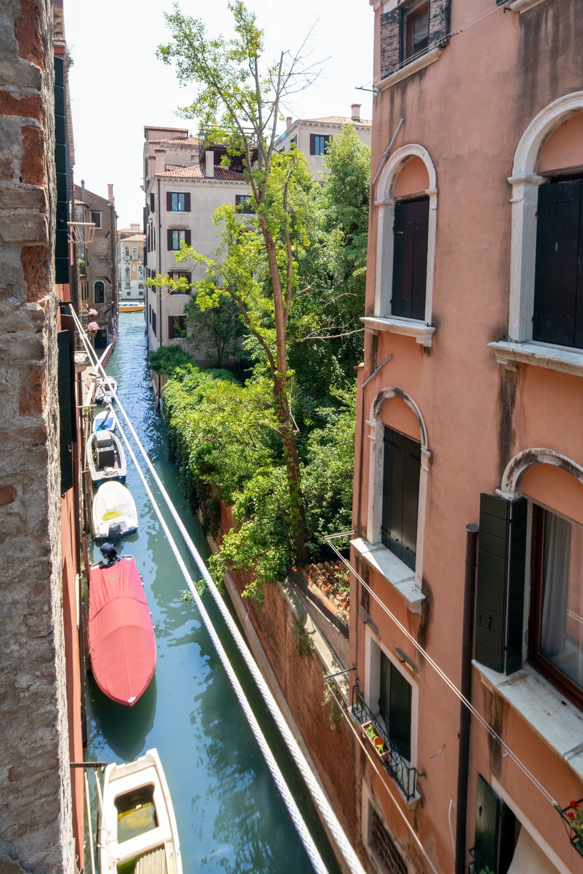 A narrow canal with boats docked on the left, flanked by buildings with balconies and windows overlooking the water.