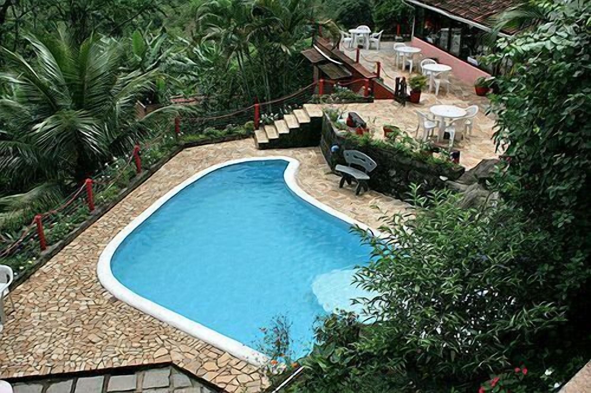 A swimming pool surrounded by stone tiles, with a patio area featuring tables and chairs.