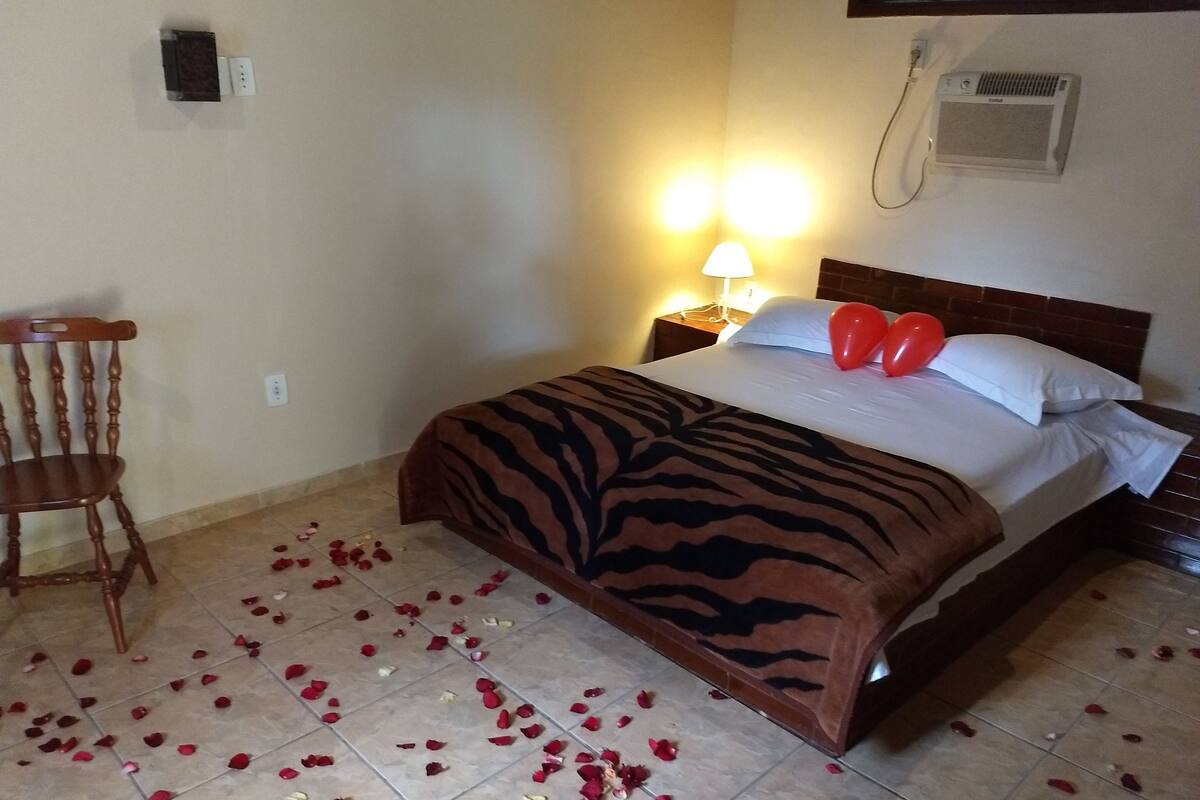 A hotel room with a bed, a chair, and a wall-mounted air conditioner.