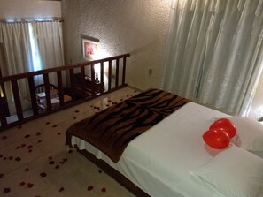 A hotel room with a bed, a zebra-patterned throw, red balloons, and scattered rose petals on the floor. - Chalé da Montanha (Duque de Caxias)