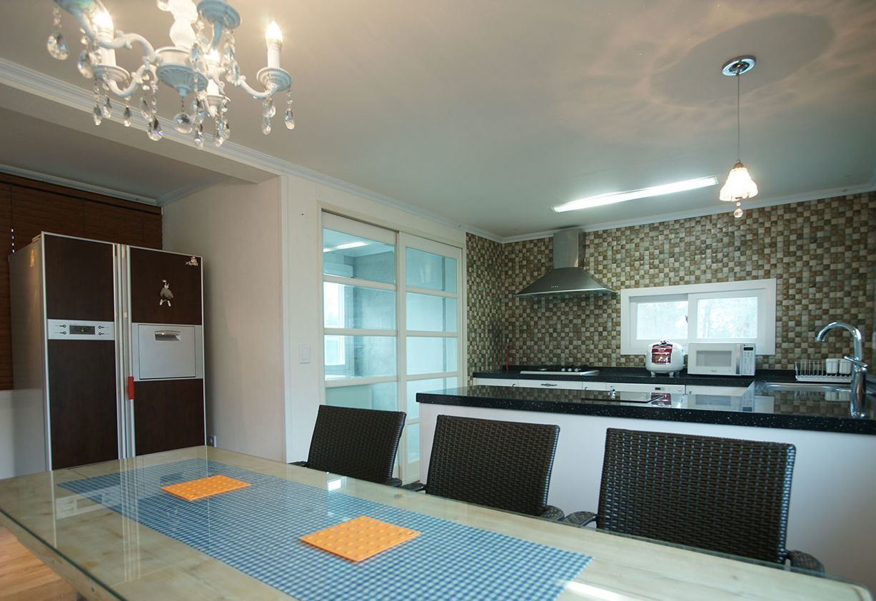 A modern kitchen with a dining area, featuring a glass-top table, chairs, a refrigerator, a microwave, and a chandelier.