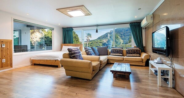 A spacious living room with a large bed, two sofas, a coffee table, and a TV. - Mirvill Pension (Seogwipo)