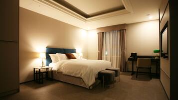 A hotel room with a bed, bedside table, lamp, chair, desk, and a mirror.