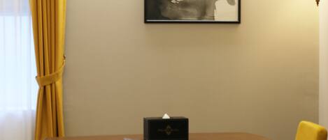A hotel room with a bed, a desk with a chair, a lamp, and a framed artwork on the wall.