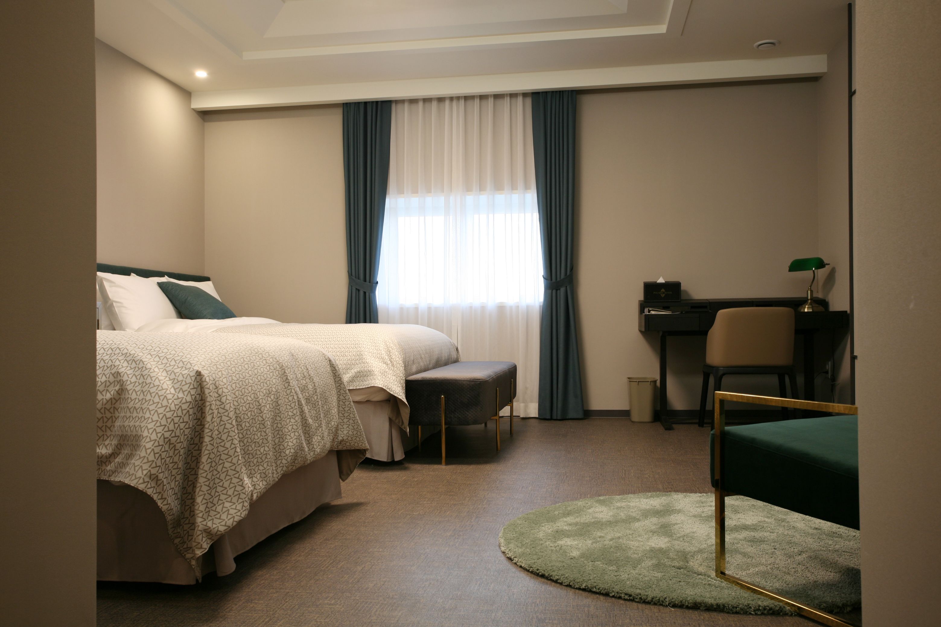 Habitación de hotel con cama, escritorio, silla y alfombra redonda pequeña.