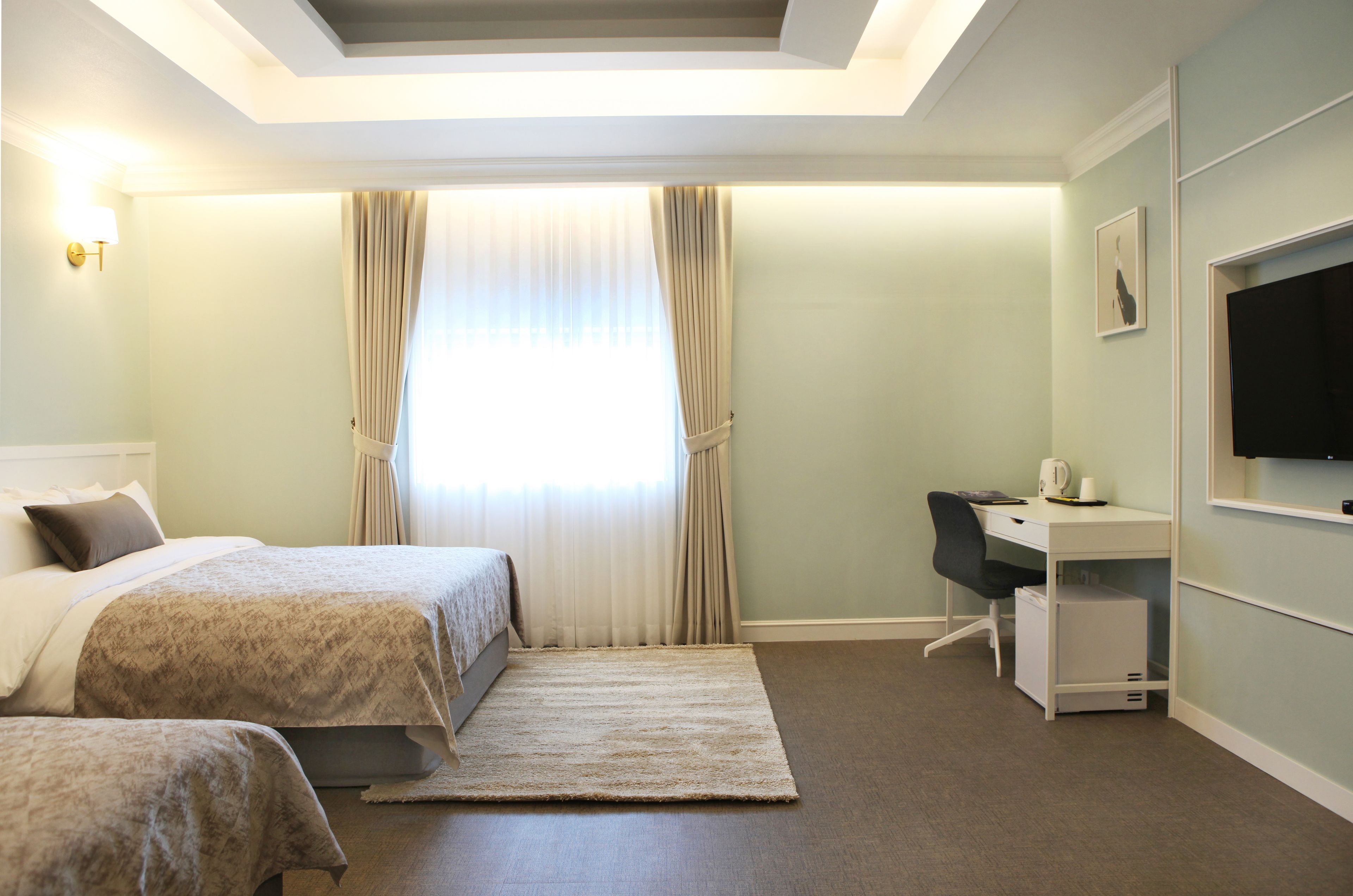 A hotel room with two beds, a desk, a chair, a TV, and a window with curtains.
