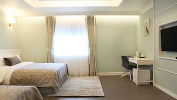A hotel room with two beds, a desk, a chair, a TV, and a window with curtains.