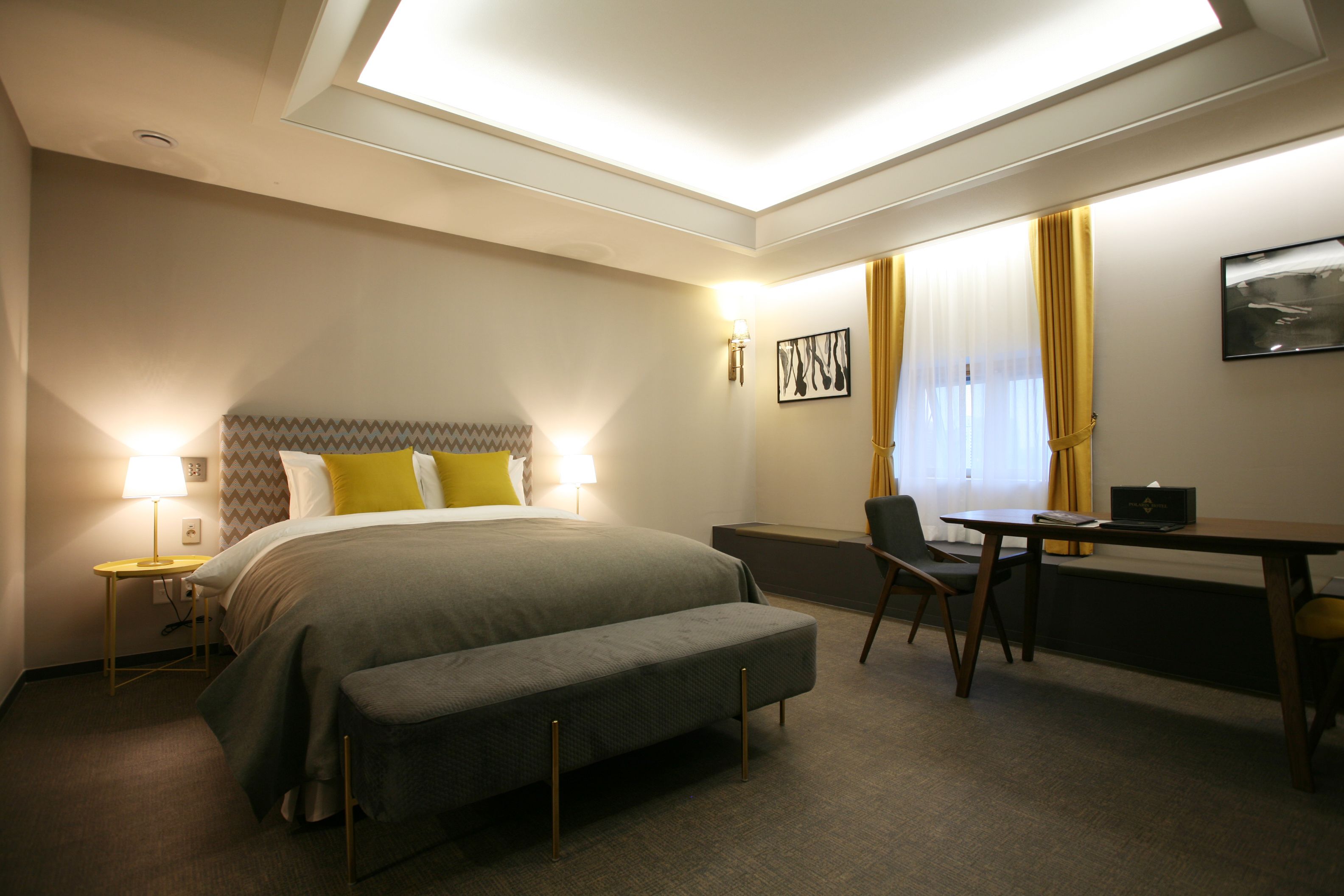 A hotel room with a bed, bedside table, desk, chair, and a bench.