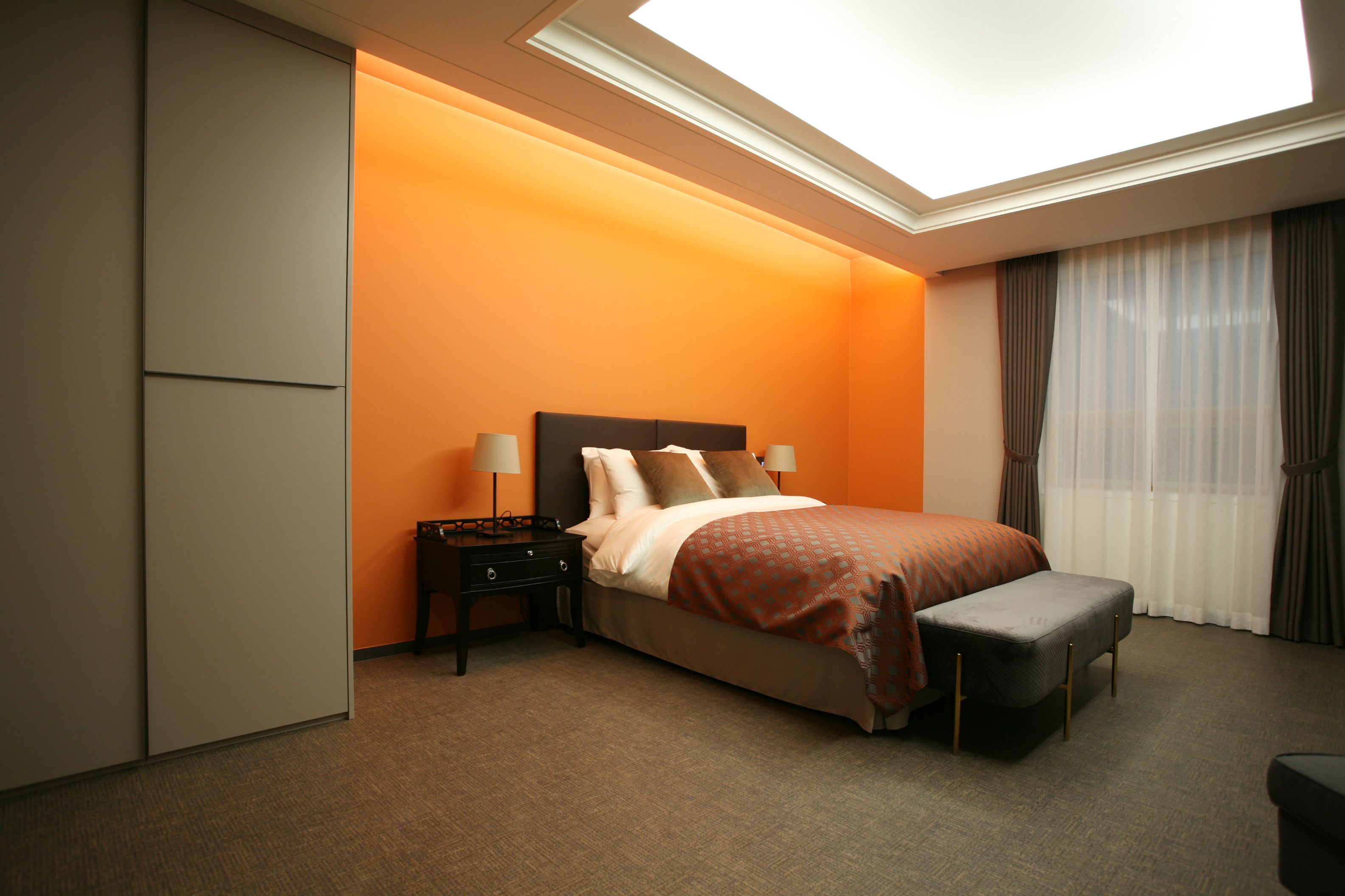Una habitación de hotel con cama, mesitas de noche, un banco, armario y tragaluz.
