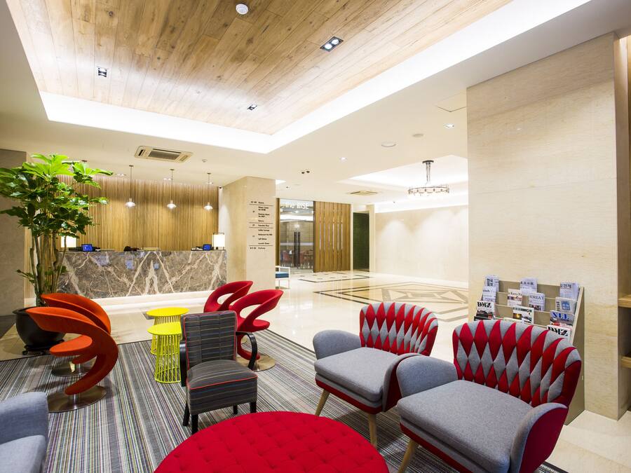 Un vestíbulo moderno con techo de madera, una recepción y varias zonas de estar con sillas de colores.