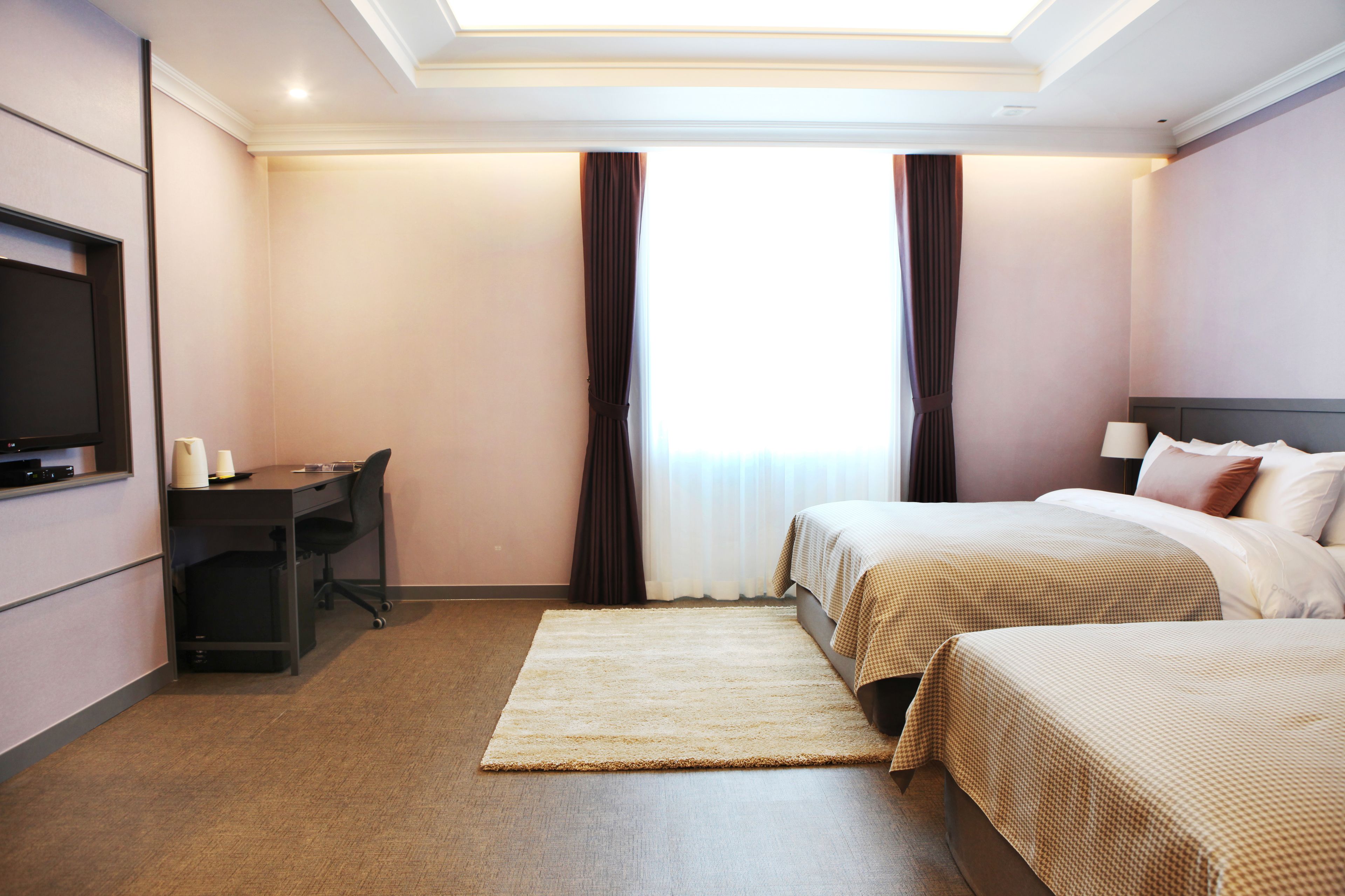 Habitació d'hotel amb dos llits, una taula de treball, televisió i una finestra gran amb cortines.