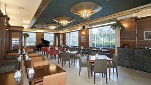 A spacious dining area with multiple tables and chairs, a grand piano, and large windows offering a view of greenery. - Polaris Hotel (Bucheon)