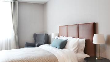 A hotel room with a bed, a chair, a lamp, and a window with curtains.