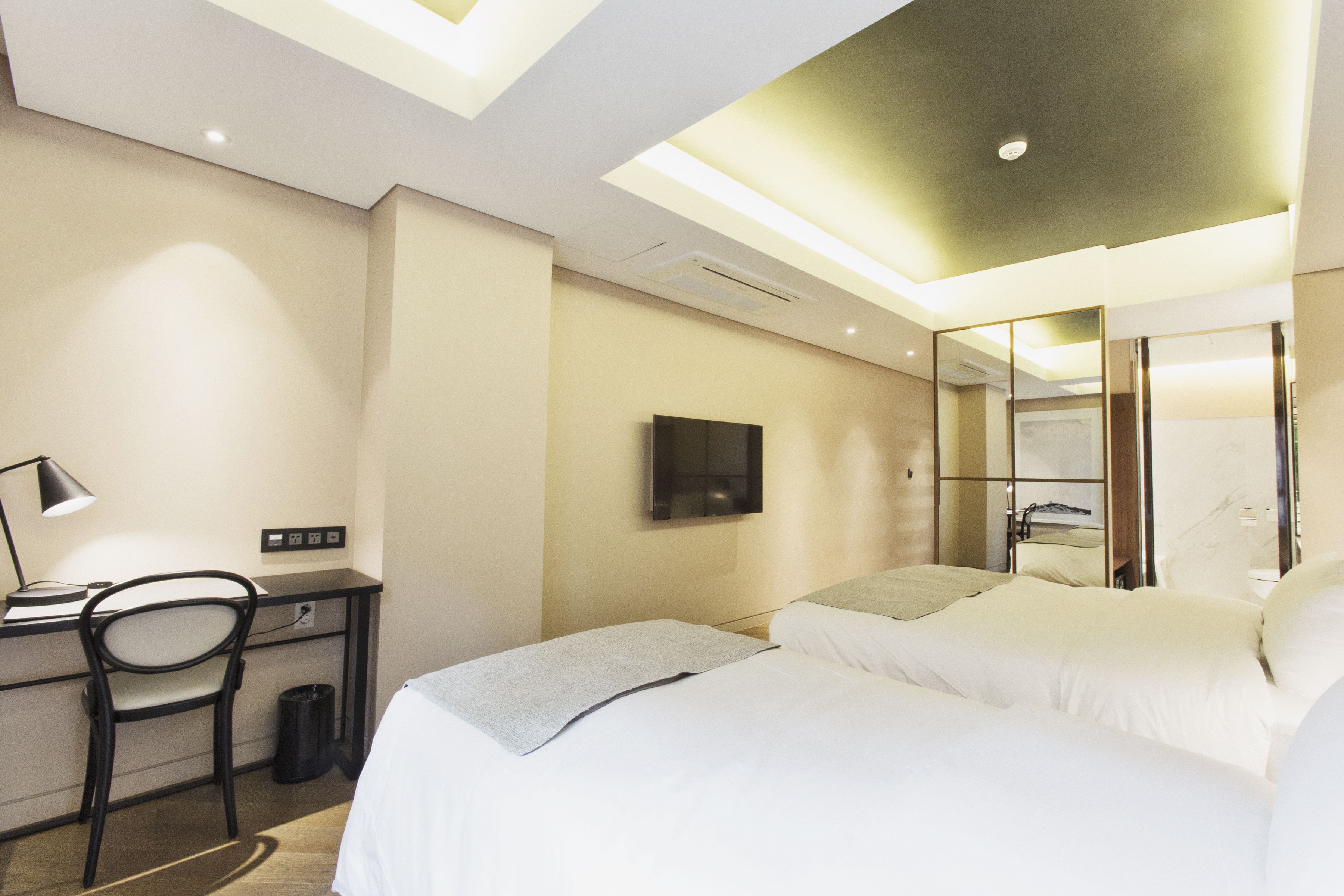 Una habitación de hotel moderna con escritorio, silla y cama con ropa de cama blanca.
