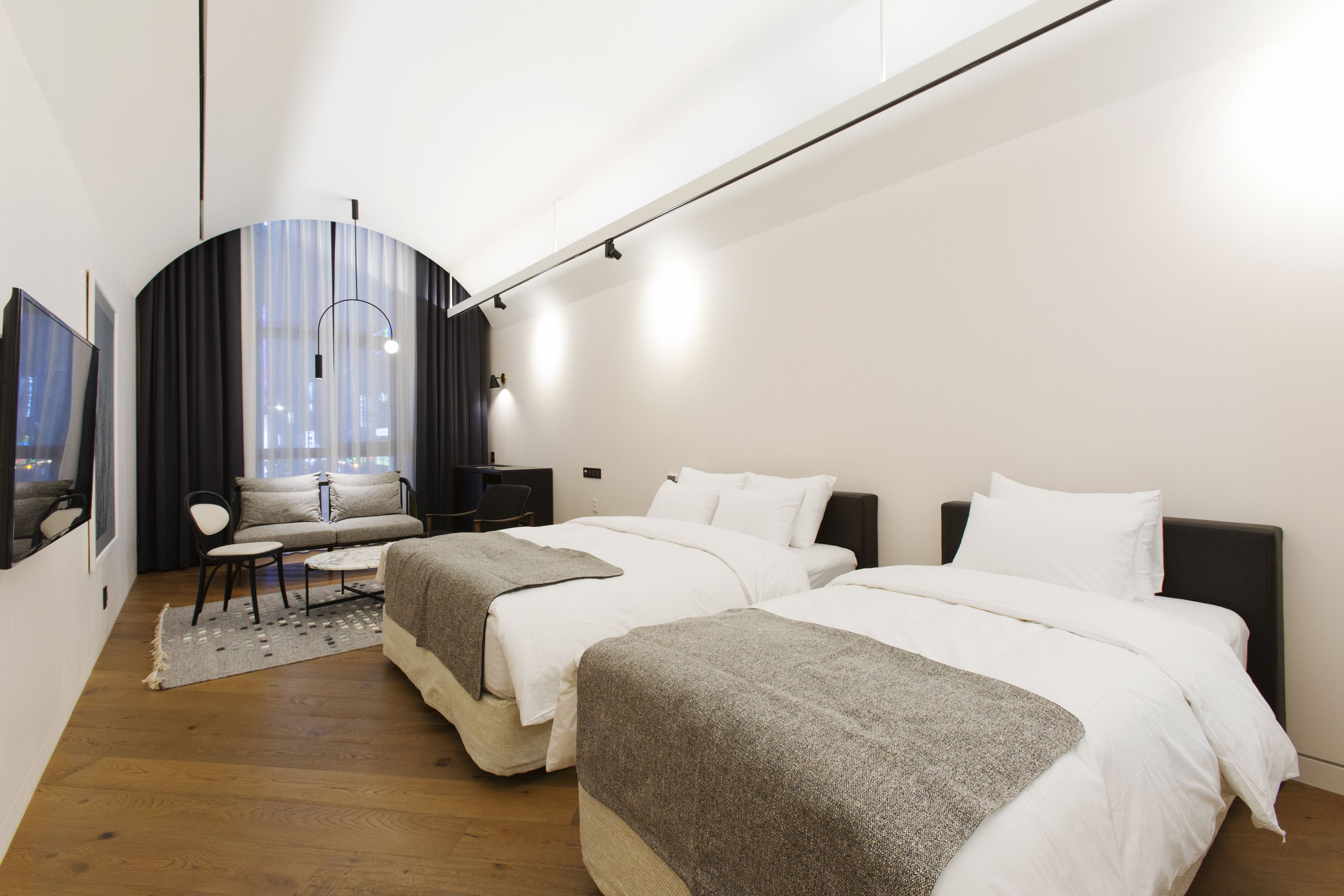 A modern hotel room with two beds, a sofa, a desk, and a city view.