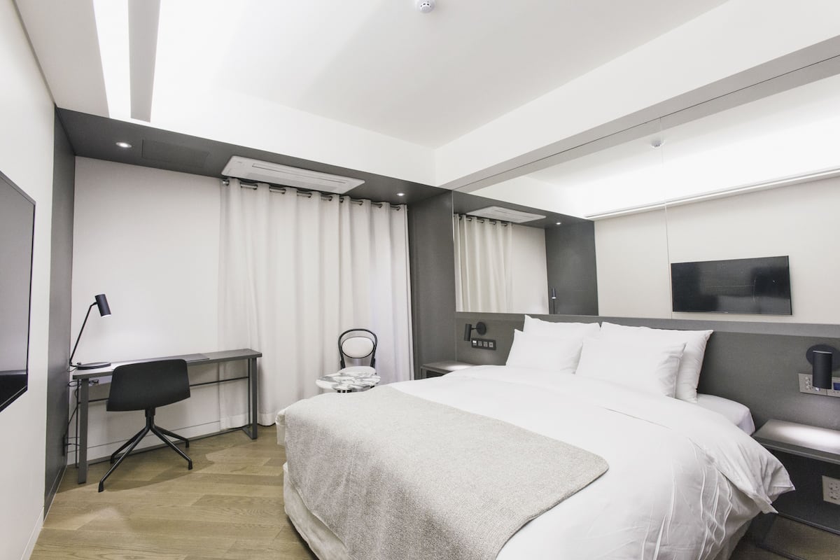 Una habitación de hotel moderna con una cama grande, un escritorio, una silla y un televisor montado en la pared.