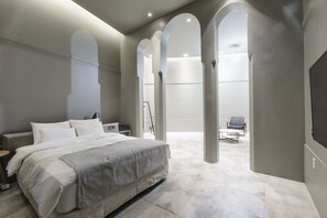 A modern bedroom with a large bed, a desk, and a chair. There are arched doorways and a view of a balcony. - GM JS Boutique Hotel (Gwangmyeong)