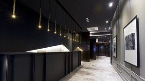 Un pasillo moderno con un mostrador de recepción negro, luces colgantes y cuadros en las paredes.