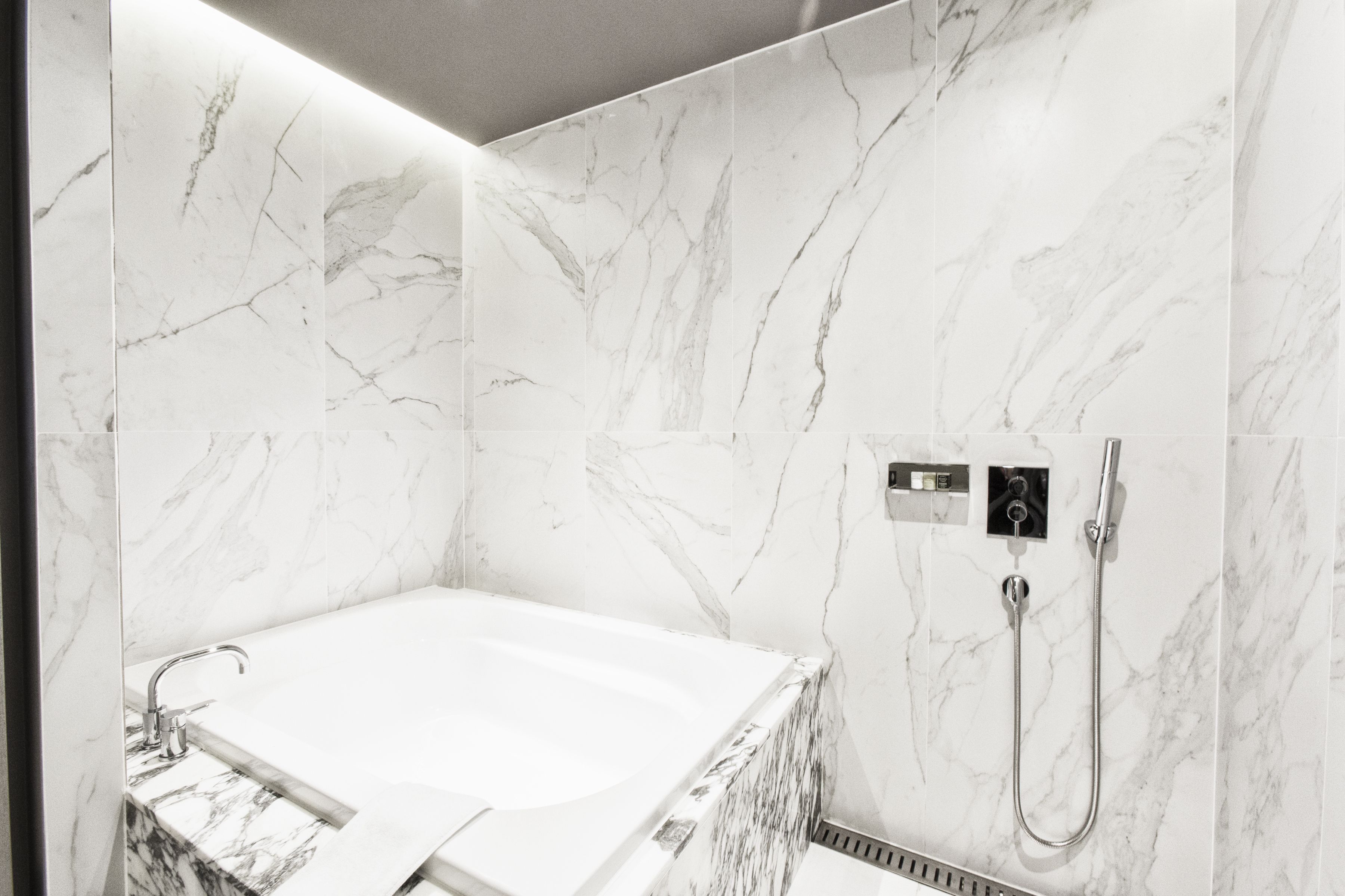 Un baño moderno con pared de mármol, una bañera, un lavabo y una ducha.