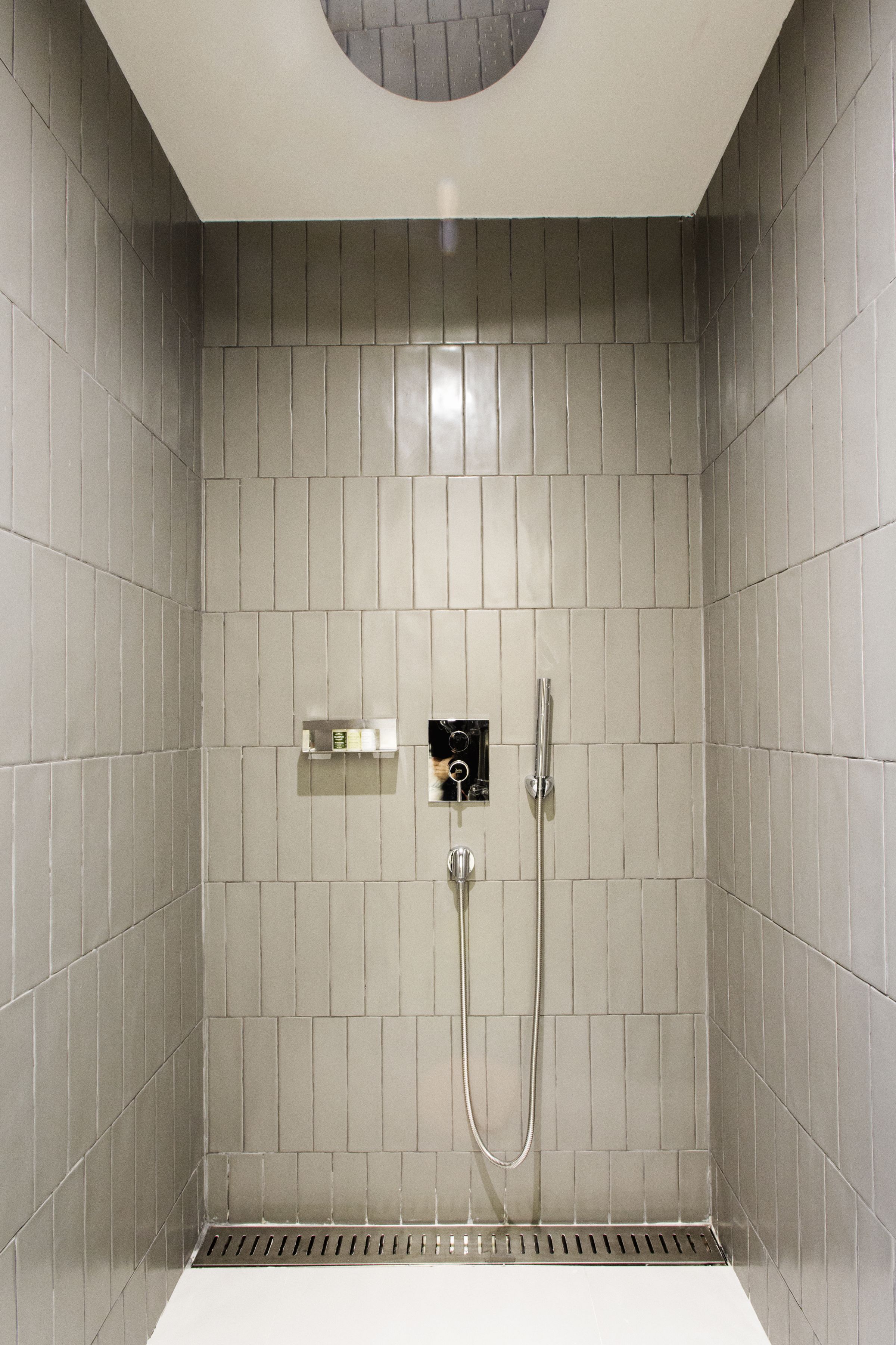 Chuveiro com azulejos cinza, painel de comando e chuveiro manual.