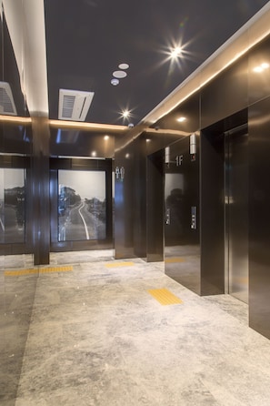 A modern elevator area with glass doors, a marble floor, and a cityscape view.