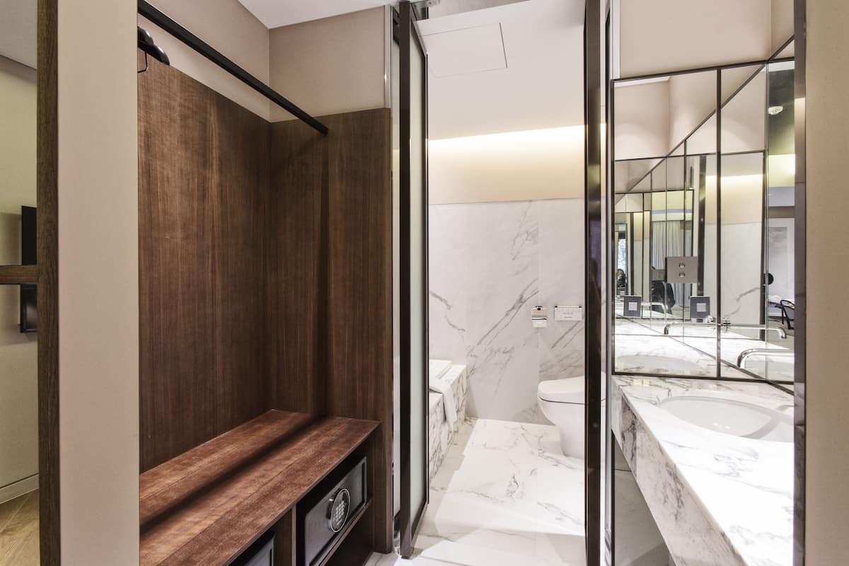 Un baño moderno con banca de madera, cabina de ducha de vidrio y lavamanos de mármol.