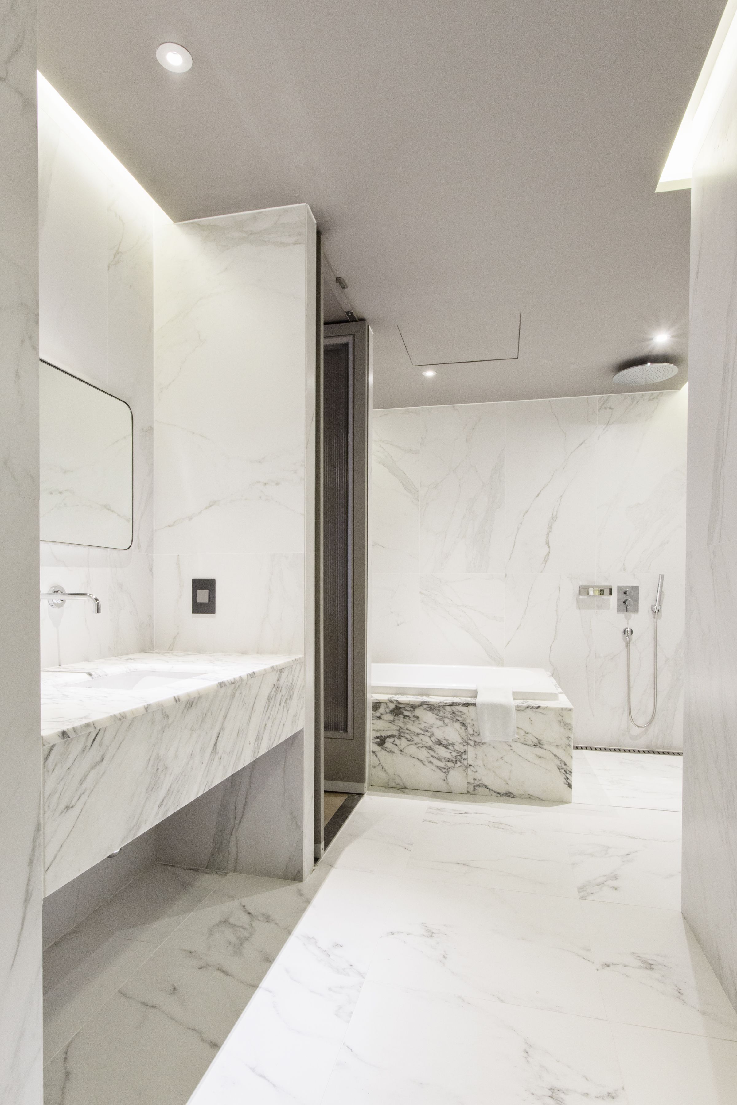 Un baño moderno con encimeras de mármol, zona de ducha y panel de control a la vista.