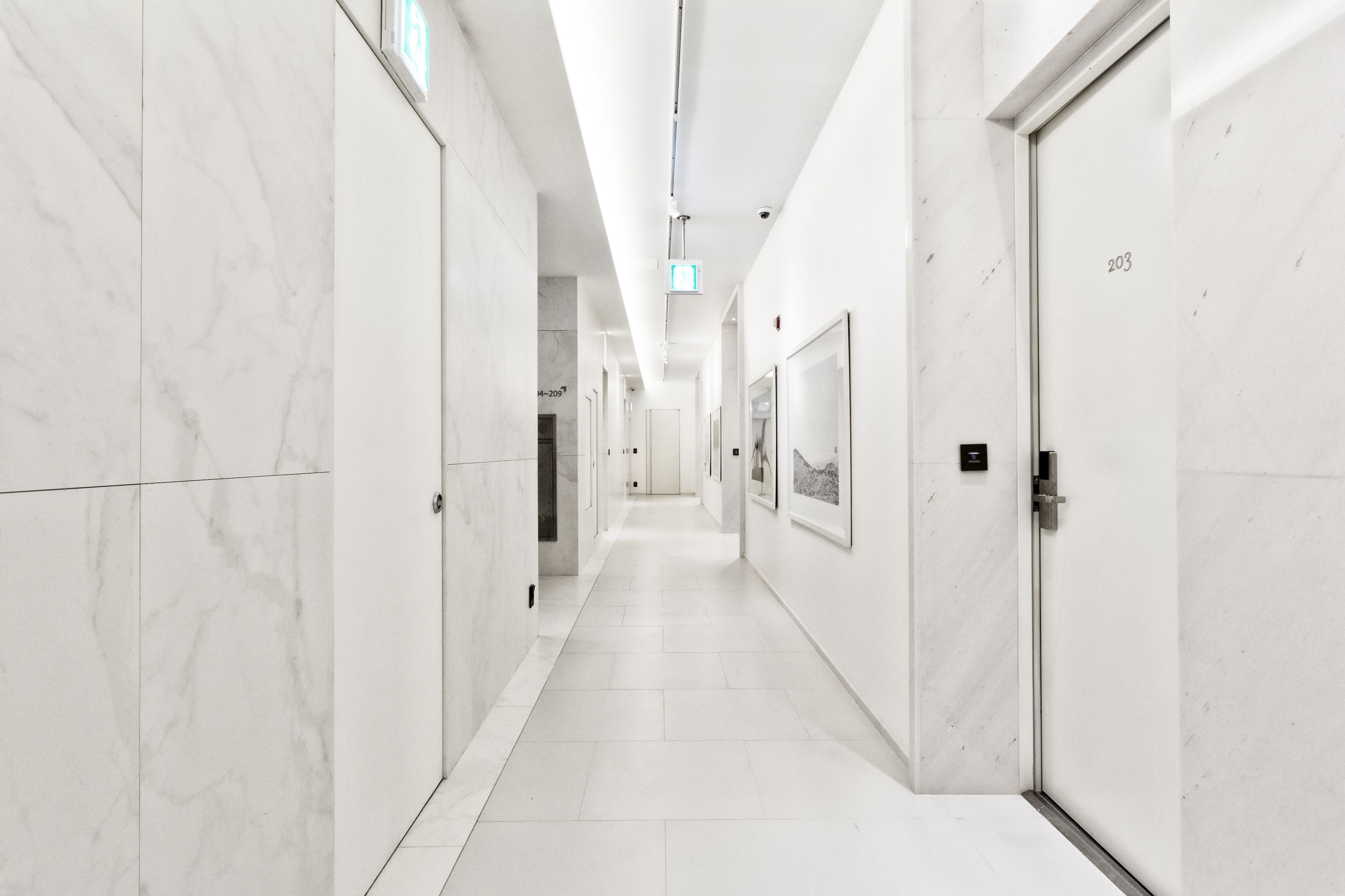 Un pasillo moderno y bien iluminado, con paredes y puertas de mármol, que conduce a varias habitaciones.