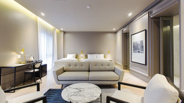 Una habitación de hotel moderna con sofá, escritorio, silla, mesa redonda y cama.