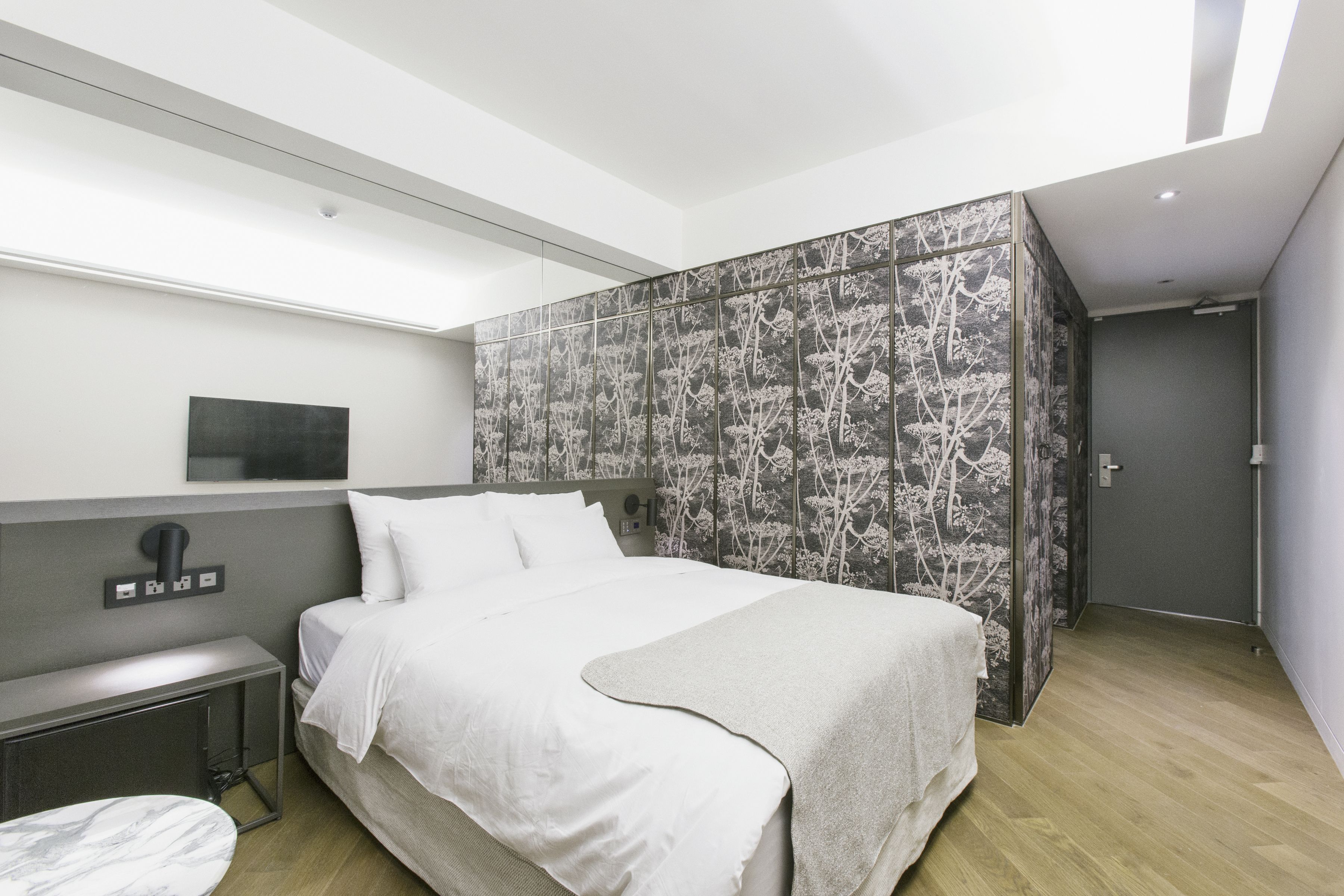 A modern hotel room with a large bed, a bedside table, and a wall-mounted TV.
