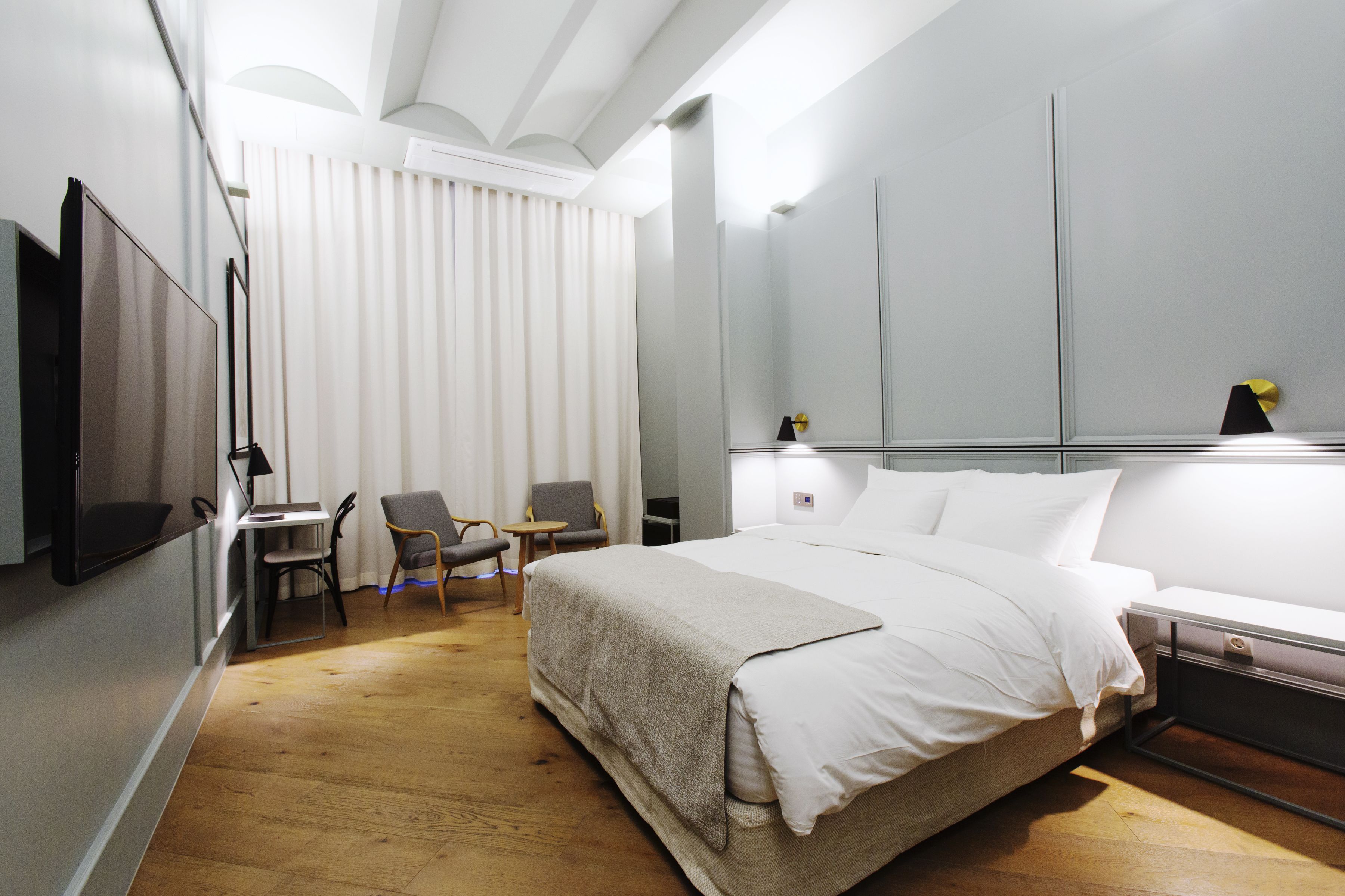 Quarto de hotel com cama, escrivaninha, cadeira, televisão e espelho.