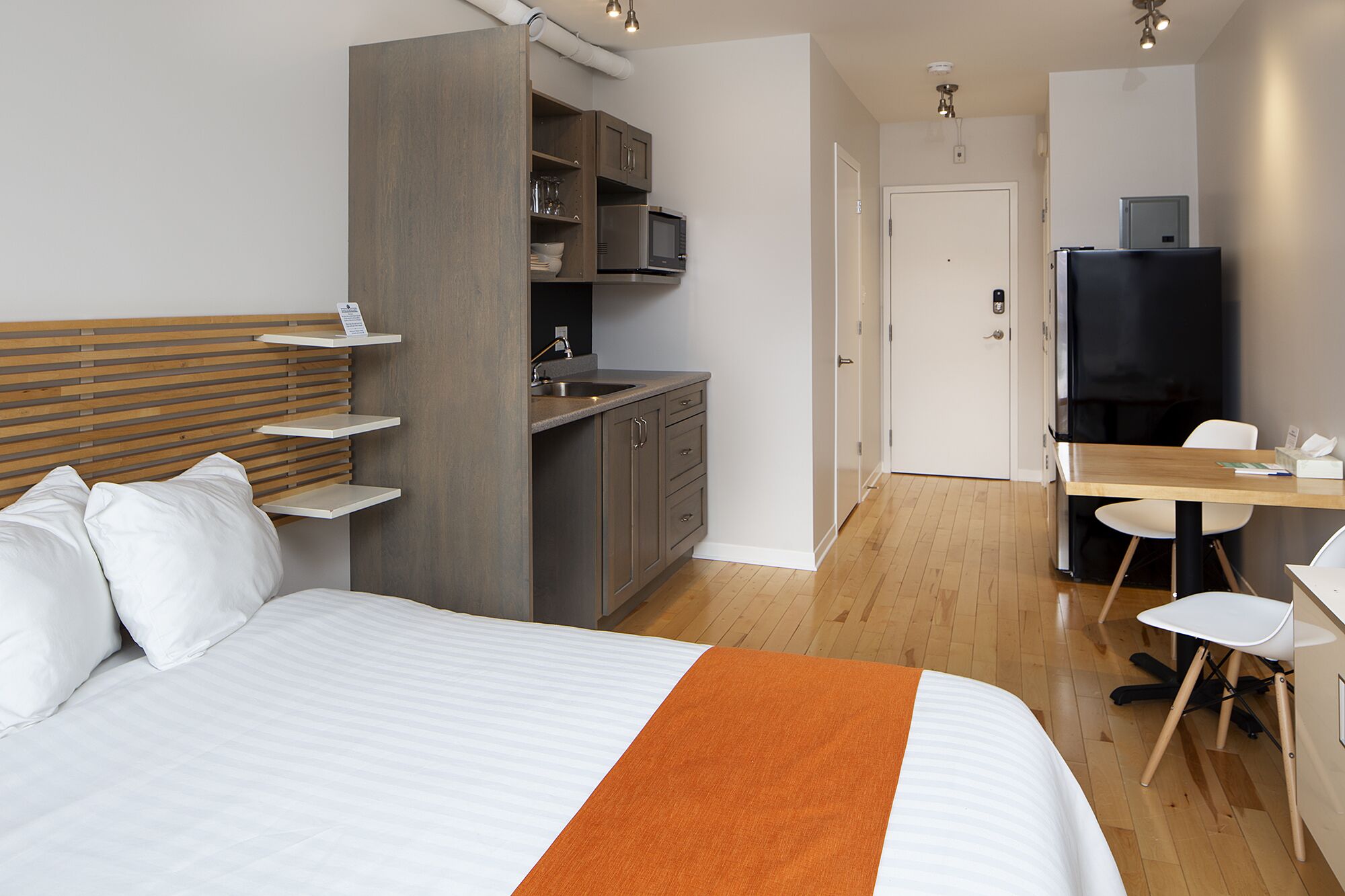 A hotel room with a bed, a desk, a kitchenette, and a TV.