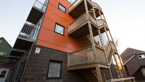 A multi-story building with a combination of brick and orange facade, wooden balconies, and a visible fire safety sign. - Micro Boutique Living - Antigonish (Antigonish)