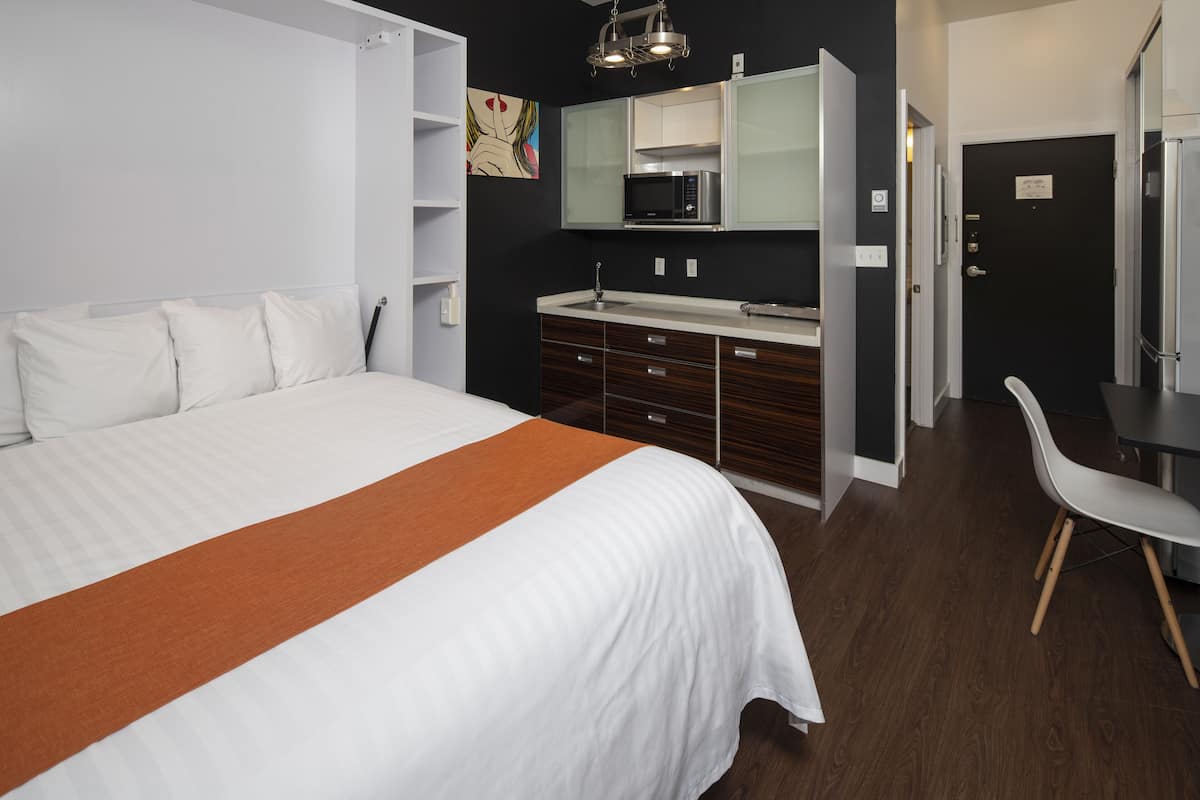 A modern hotel room with a large bed, a built-in desk, a microwave, and a chair.