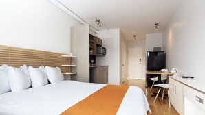 A hotel room with a bed, a desk, a chair, a TV, and a kitchenette. - Micro Boutique Living - Antigonish (Antigonish)
