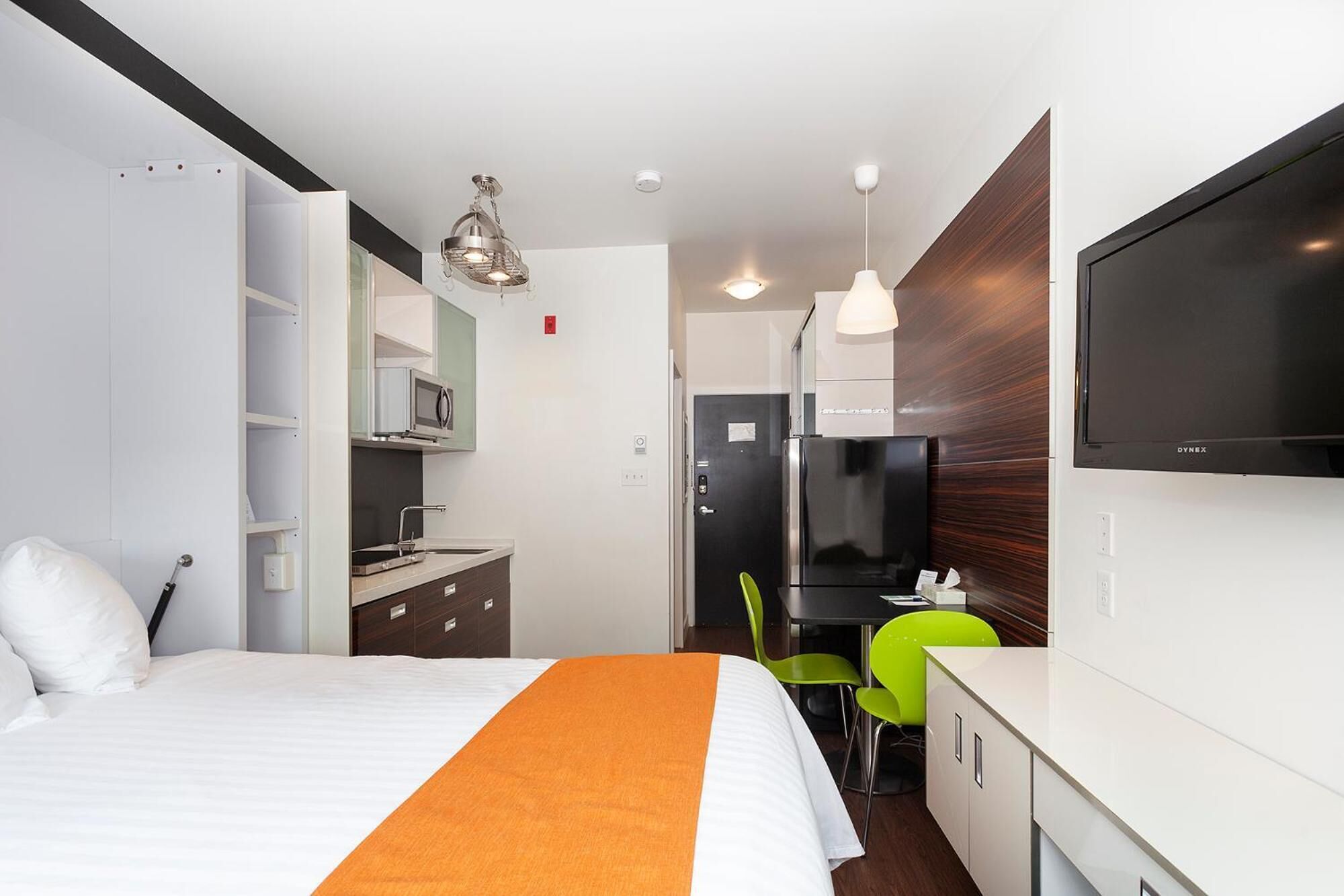 A hotel room with a bed, a desk, a microwave, a refrigerator, and a TV.