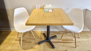 A small, rectangular wooden table with a black metal base, flanked by two white chairs. A tissue box and a sign indicating a non-smoking room are on the table. - Micro Boutique Living - Antigonish (Antigonish)