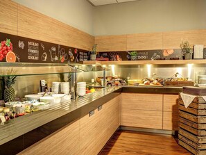 A breakfast buffet with various food items, a glass display case, and wooden cabinetry. - ibis München City Süd (Munich)