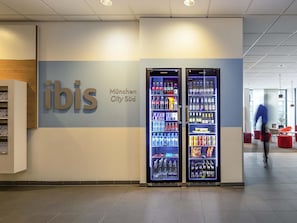 A vending machine area with a sign for 'ibis München City Süd' and a person walking in the background. - ibis München City Süd (Munich)