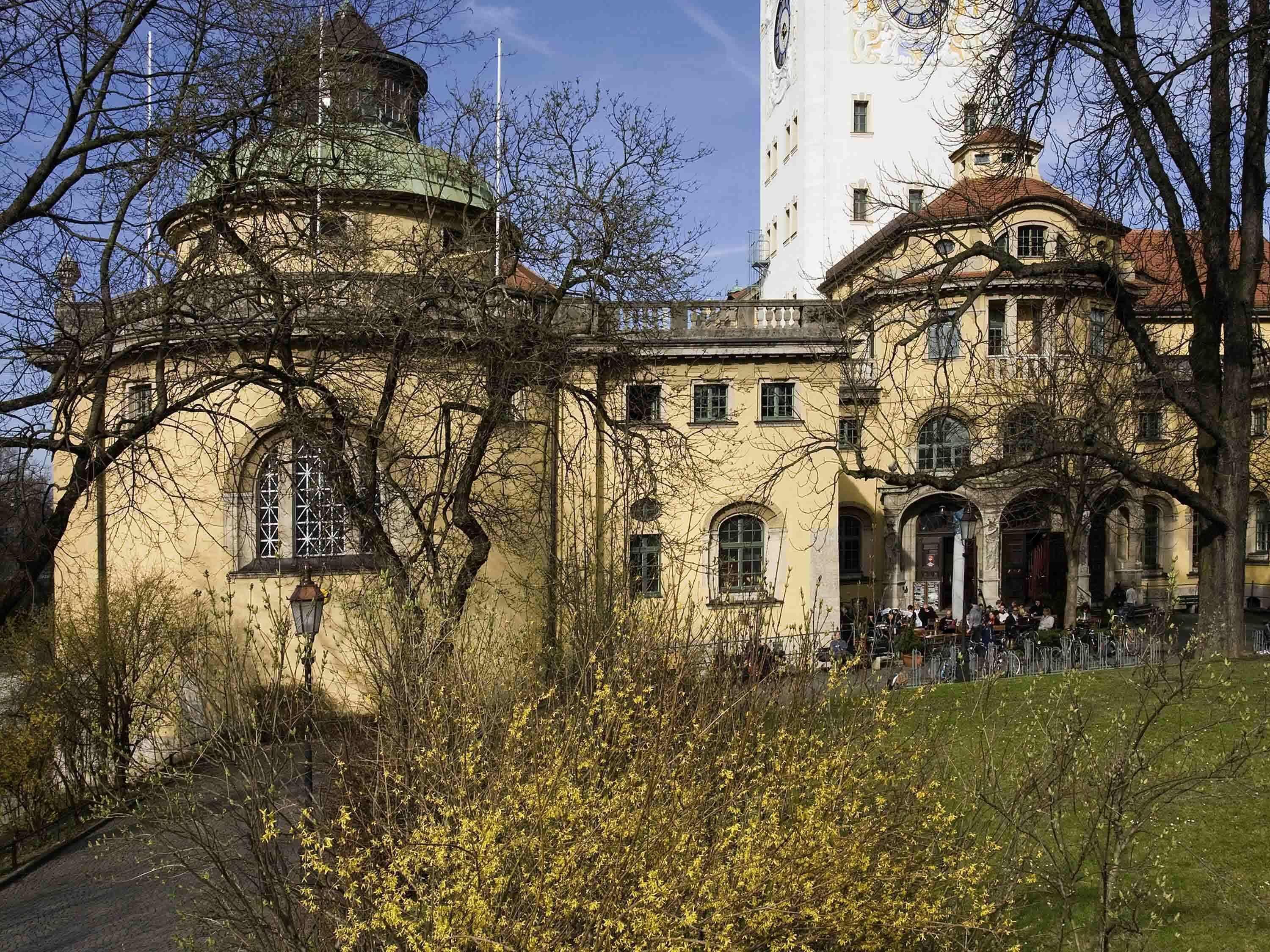 A historic building with a dome and arched windows, surrounded by trees and a clear sky.
