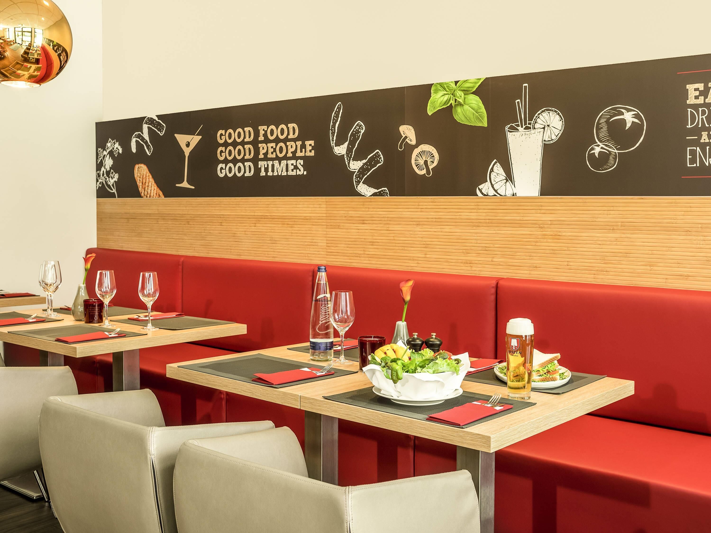 A restaurant interior with red booths, wooden tables, and a wall mural with food and drink illustrations.