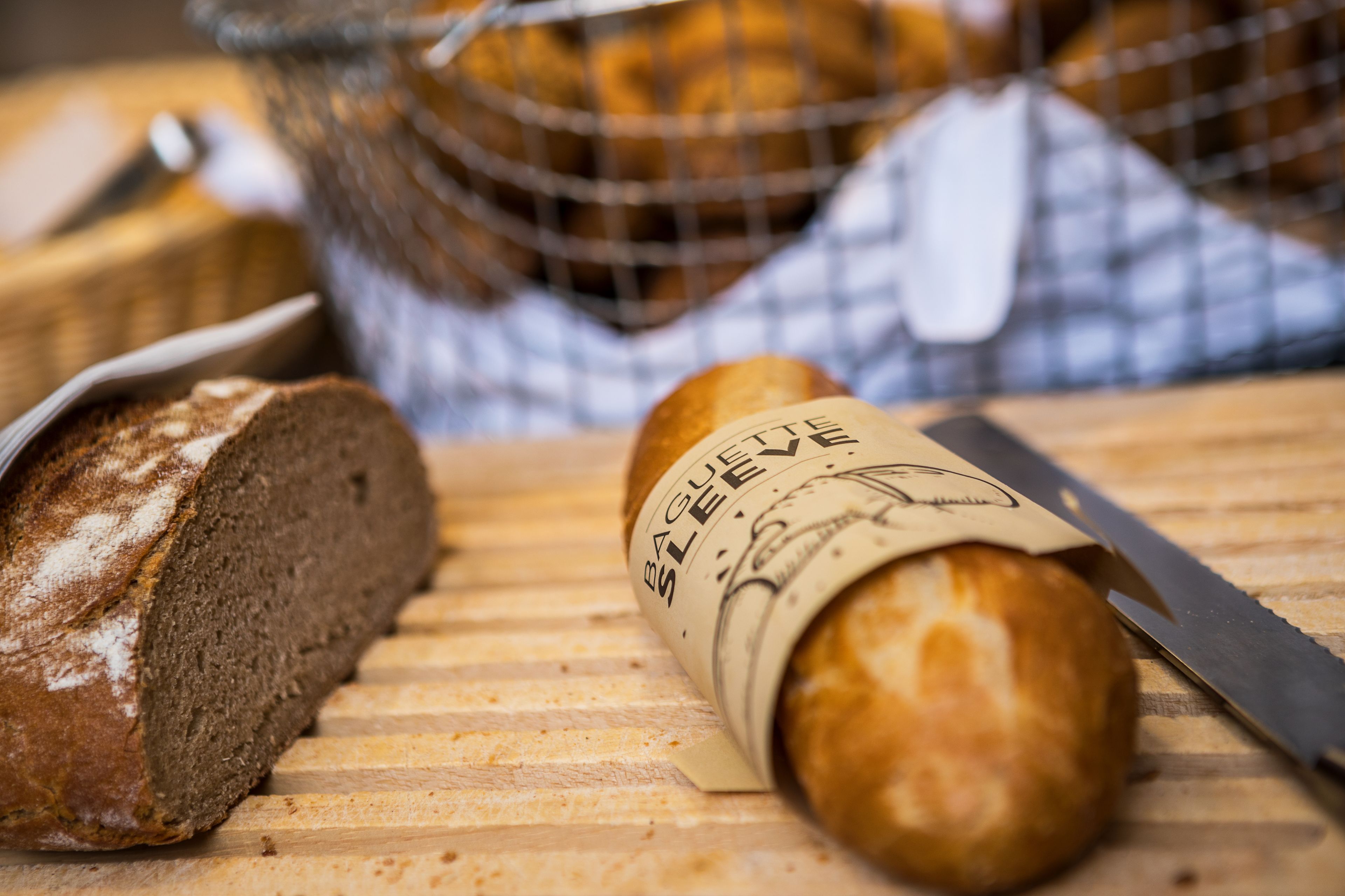 A loaf of bread with a label, a knife, and a basket of bread in the background.