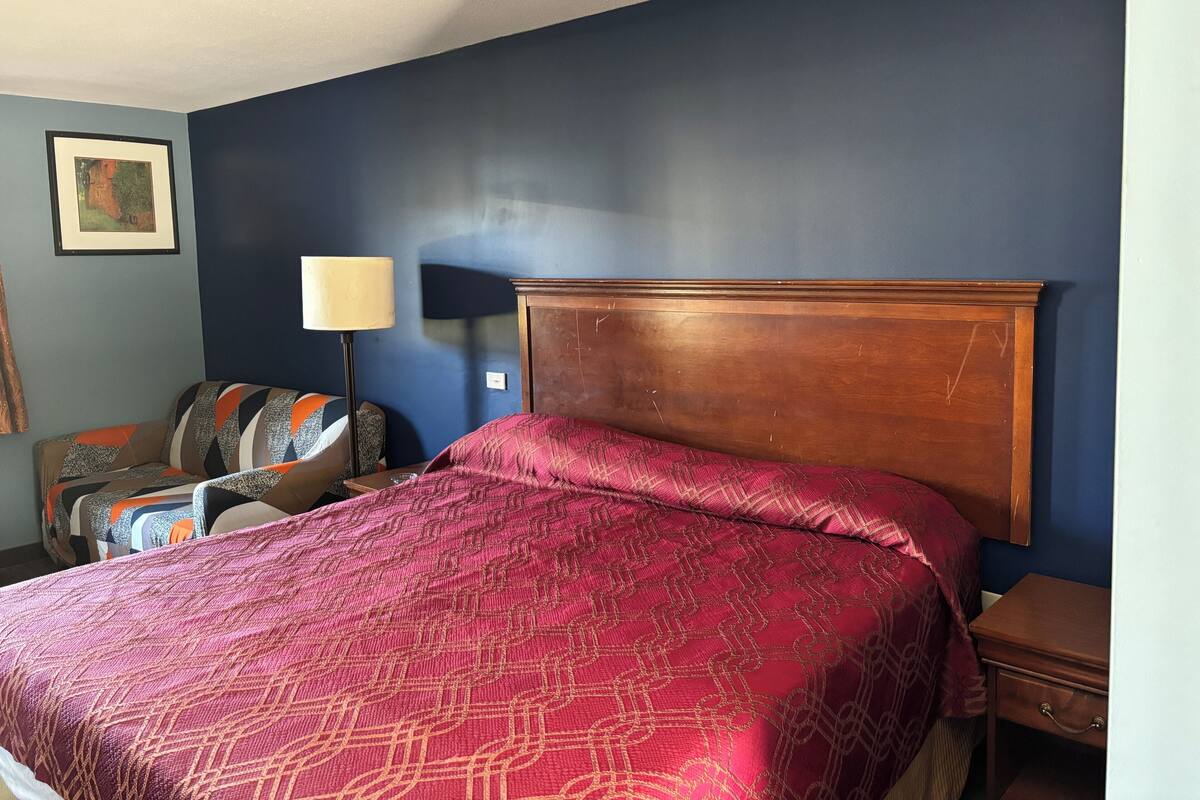 A bedroom with a large bed, a nightstand, a lamp, and a chair.