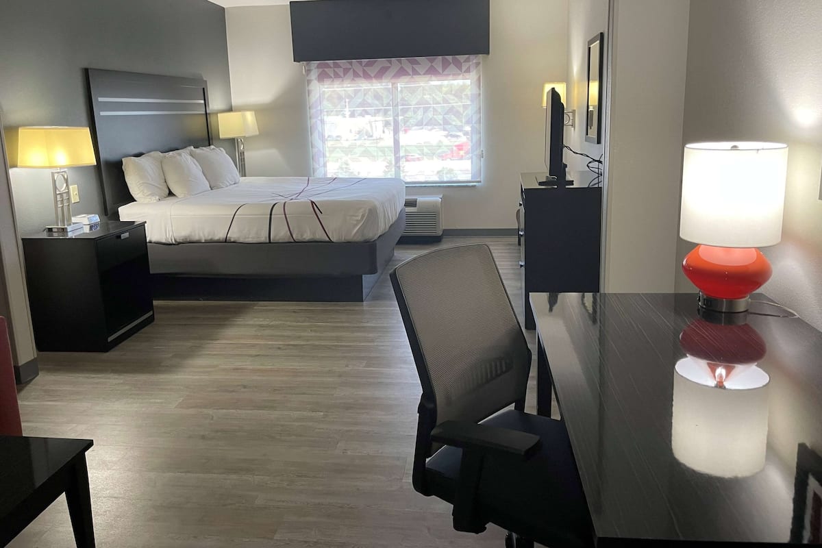 A hotel room with a bed, bedside tables, a desk, a chair, a TV, and a window with a view.