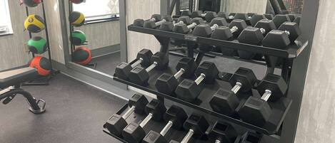 A gym with multiple sets of dumbbells arranged on racks, a treadmill, and exercise balls.